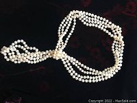Long strand of white cultured freshwater pearls shown arranged on a black surface, showing length and pearl uniformity.