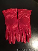 Pair of small red genuine leather ladies gloves laid flat showing heart embossed detail on back of hands.