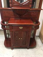 Front view of solid mahogany hallway stand showing carved mirror, shelf, drawer with brass handle, rounded side rails, and double door cabinet with carved panels.