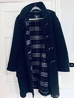 Full view of the black wool Burberry winter coat hanging on a door, showing the plaid interior lining and toggle closures.