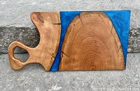 Front view of large cherry wood board with blue epoxy resin river accent and integrated handle, background concrete surface