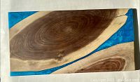 Top-down view of single live edge walnut board with teal resin sections on white background