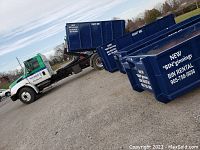 Photo of a large blue 14-yard waste bin with company branding beside a truck labeled 'New Roots Tree and Recycling' with contact info, showing the bin rental unit.