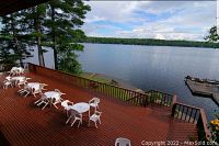 Outdoor lakeside deck with multiple white plastic tables and chairs overlooking the lake