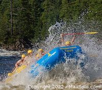 Group of rafters paddling a blue Wilderness Tours raft through river rapids with water splashing