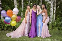 Four women in formal prom dresses posing outdoors with balloons