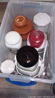 Top-down photo of bin filled with various glass canisters, bakeware pieces, and kitchen storage containers.