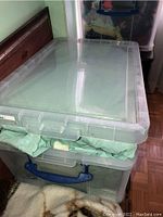 Stacked plastic bins with green fabric visible in the top bin, likely the coverlet and pillows.