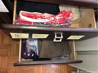 Top drawer with bags and folded clothing items, some partially visible