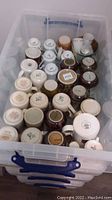 Plastic storage bin filled with assorted ceramic mugs, viewed from above showing bases and handles.