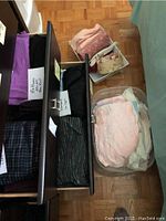 Two drawers filled with various pajama bottoms in different colors and patterns, and bins with folded night gowns and toiletry bags nearby on the floor.