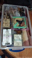 Overview of plastic tote with assorted religious decor, crosses, plaques, statues, and boxed items wrapped in plastic bags and foam.