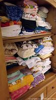 Multiple shelves filled with folded towels, tablecloths, and blankets of various colors and patterns, tightly stacked.