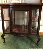 Front view showing curved glass panel, beaded trim and cabriole legs