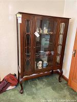 Full front view of antique wooden china cabinet with glass doors and legs on carpeted floor.
