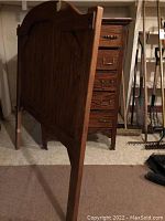 Side view of the oak dresser showing five drawers with metal handles and the twin headboard behind it.