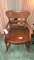 Front view of antique oak rocking chair showing wide backrest, armrests, and contoured seat with some scuff marks.