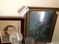 Photo showing both art pieces side by side, with an oil lamp and another glass item in front.