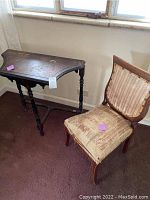 Photo showing the antique side table and chair side by side, highlighting table's shape and chair's upholstery condition.