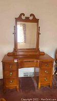 Full view of antique wooden vanity with attached mirror, shown against a wall with carpeted floor