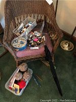 Chair with wicker platter holding assorted buttons, plastic box of buttons, and umbrella leaning against chair with yarn and crochet hooks on floor.