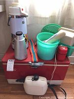 Photo shows the full set of camping and picnic items including red Coleman cooler base with colorful strap, thermoses, green bucket, white container, and red insulated container.