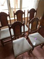 Full view of five vintage oak dining chairs arranged in the room near a window, showing the carved wooden backs and upholstered seats.