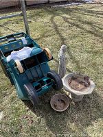 Full view showing an upside down green garden cart, Saint Francis statue, birdbath, and two planters on grass