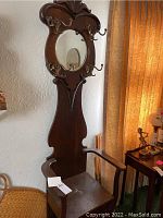 Front view of wooden hall tree featuring carved crest top, oval mirror, multiple brass hooks and integrated seat