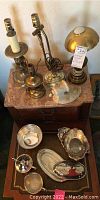 Overview photo showing five silver-plate items on a table drawer and five small lamps placed on the top surface of a wooden piece of furniture.