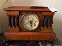 Full frontal view of antique Seth Thomas mantle clock showing wooden body, black columns, brass bezel with floral decoration and clock face.