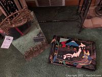 Small brass table mirror with ornate brass frame and stand next to Japanese photo album on carpeted floor.