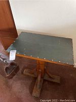 View of the table showing the rectangular, dark metal top with metal tacks around the edge and part of the wooden base.