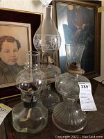 Three glass oil hurricane lamps arranged together, showing metal wick holders and etched glass on one chimney.
