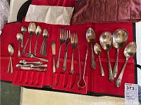 Full spread of silver-plated utensils on a red fabric roll case, showing various spoons, forks, knives, tongs, and serving pieces.