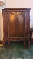 Front view of small antique wooden china cabinet showing carved details, double doors, and legs with heavy finish damage and scratches.