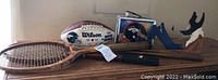 Wide view of all sports items including football, tennis racquets, wooden figures, baseball bat and stand