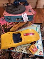 Yellow Barbie Remote Control Super Vette toy car on a board game, with wired remote control and small vintage record player in the background.