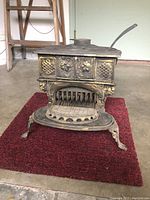 Front view of the antique cast iron wood stove showing decorative floral and lattice design on the door and curved legs.