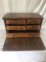 Front view of the wooden antique tool cabinet with drawers labeled for staples, jigsaw blades, and fuses.