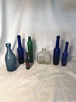 Seven antique glass bottles arranged side by side showing color and shape differences.