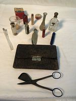 Photo showing the full antique medical kit including the leather case, various glass bottles, container, and metal instrument with magnifying lens, arranged on a white surface.