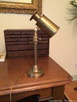 Full side view of vintage brass desk lamp on wooden desk with adjustable shade and power cord.