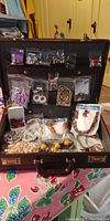 Full view of the open attaché case filled with assorted costume jewelry packed in plastic bags and small packets attached to the case lid
