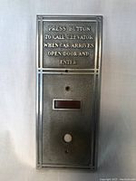Front view of vintage solid metal elevator call button showing engraved text and button hole.