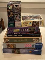 Stacked boxed puzzles showing titles, brands, and piece counts
