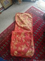 Quilted bedspread folded and laid on patterned red rug showcasing copper and yellow floral design and some edge wear.