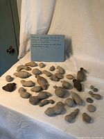 Photo displaying a large number of natural forming concretions identified as 'Fairy Stones' placed on a white cloth surface, showing their varied shapes and sizes.