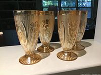 Four Marigold Carnival Glass footed tumblers with embossed Iris & Herringbone floral pattern shown together on a white surface.