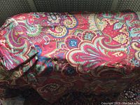 Photo showing the colorful paisley patterned fabric of the duvet cover and shams draped over a surface with a visible textile texture and colors of red, green, blue, and yellow.